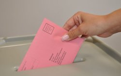 Foto zeigt eine Hand, die einen Wahlschein in die Wahlurne steckt.