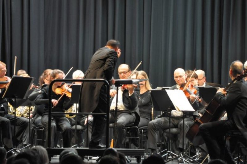Das Foto zeigt den Dirigenten und die Musiker der Neuen Philharmonie Westfalen auf der Bühne der Jungholzhalle.