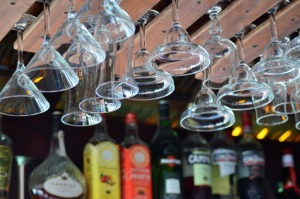 Foto zeigt den oberen Bereich einer Cocktailbar mit diversen Spirituosen im Hintergrund und Cocktailgläsern an Gläserschienen im Vordergrund