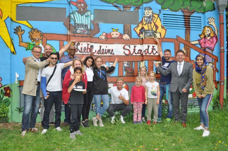 Foto zeigt den Ersten Beigeordneten Holger Jung und die Akteure der Graffitiaktion vor dem Kunstwerk.